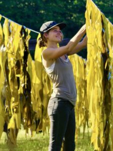 Woman hangs seaweed with lines of kelp on either side of her.