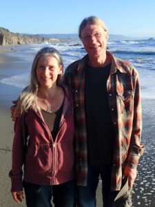 Co-founders James and Kari looking at the camera and smiling, on the beach in northern california.