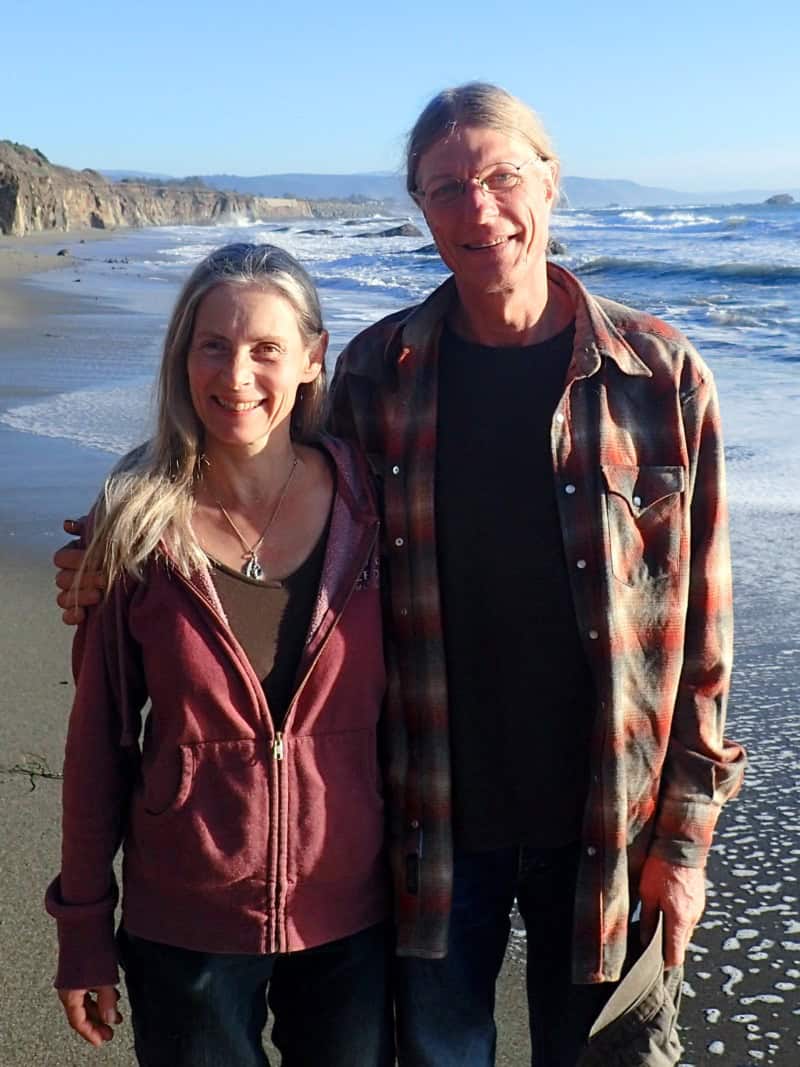 Co-founders James and Kari looking at the camera and smiling, on the beach in northern california.