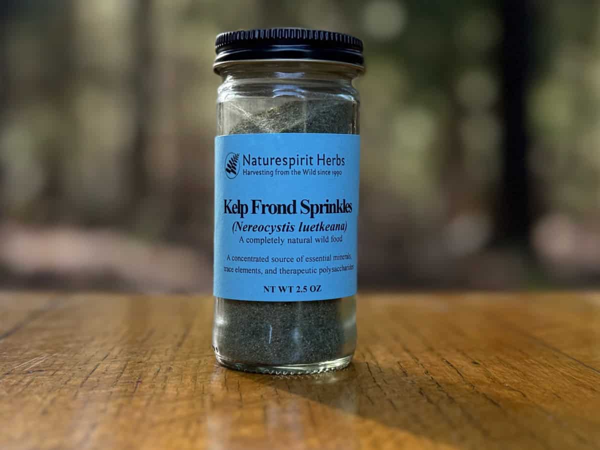 Kelp frond sprinkles in a glass bottle on a wooden table, photo taken with outdoor, natural light.